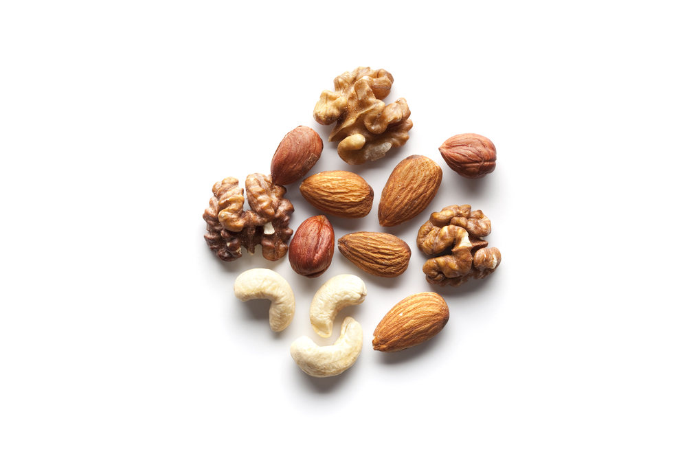Vit bakgrund med olika nötter på som är utmärka nyttiga snacks att äta för att minska ett midjemått